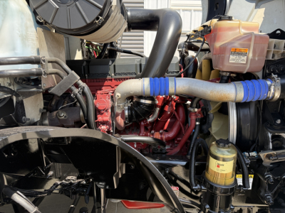 Engine bay of a 2021 Mack AN64T conventional daycab showing red engine block, blue silicone hoses, intake tubing, and coolant reservoir.