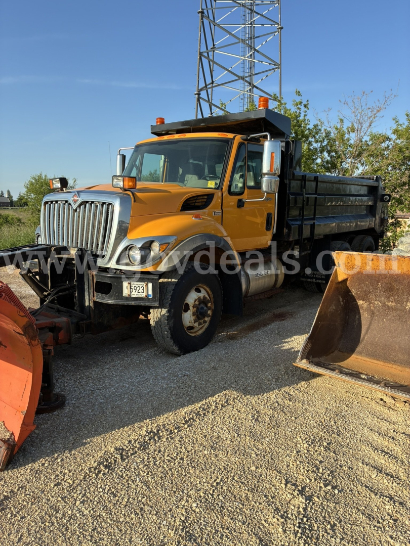 Front left view of a yellow International 7400 dump truck with plow equipment, side mirrors, and black dump bed.