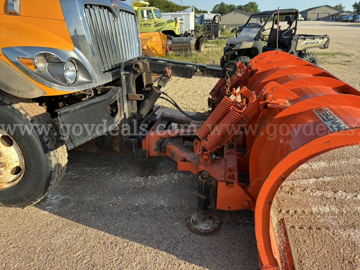 Front left view of a 2009 International 7400 dump/plow truck with an orange snow plow attachment connected to the frame; visible wheels, grille, and hydraulic components.