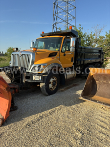 Front left view of a yellow International 7400 dump truck with plow equipment, side mirrors, and black dump bed.