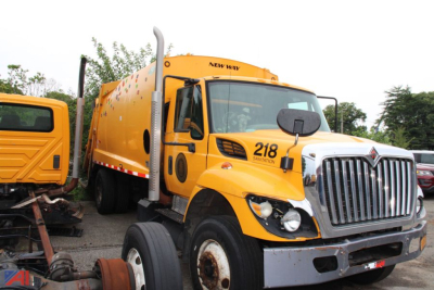 Truck cab of a yellow 2013 International WorkStar 7300 Packer with front grille and windshield, showing '218' on door and New Way unit on top.