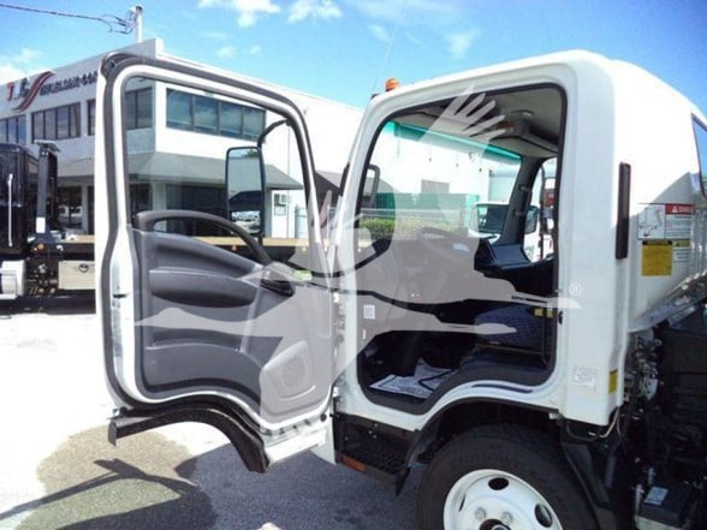 Isuzu NPR HD cab interior with both doors open, showing steering wheel, seat, and dashboard; white exterior and truck chassis visible.