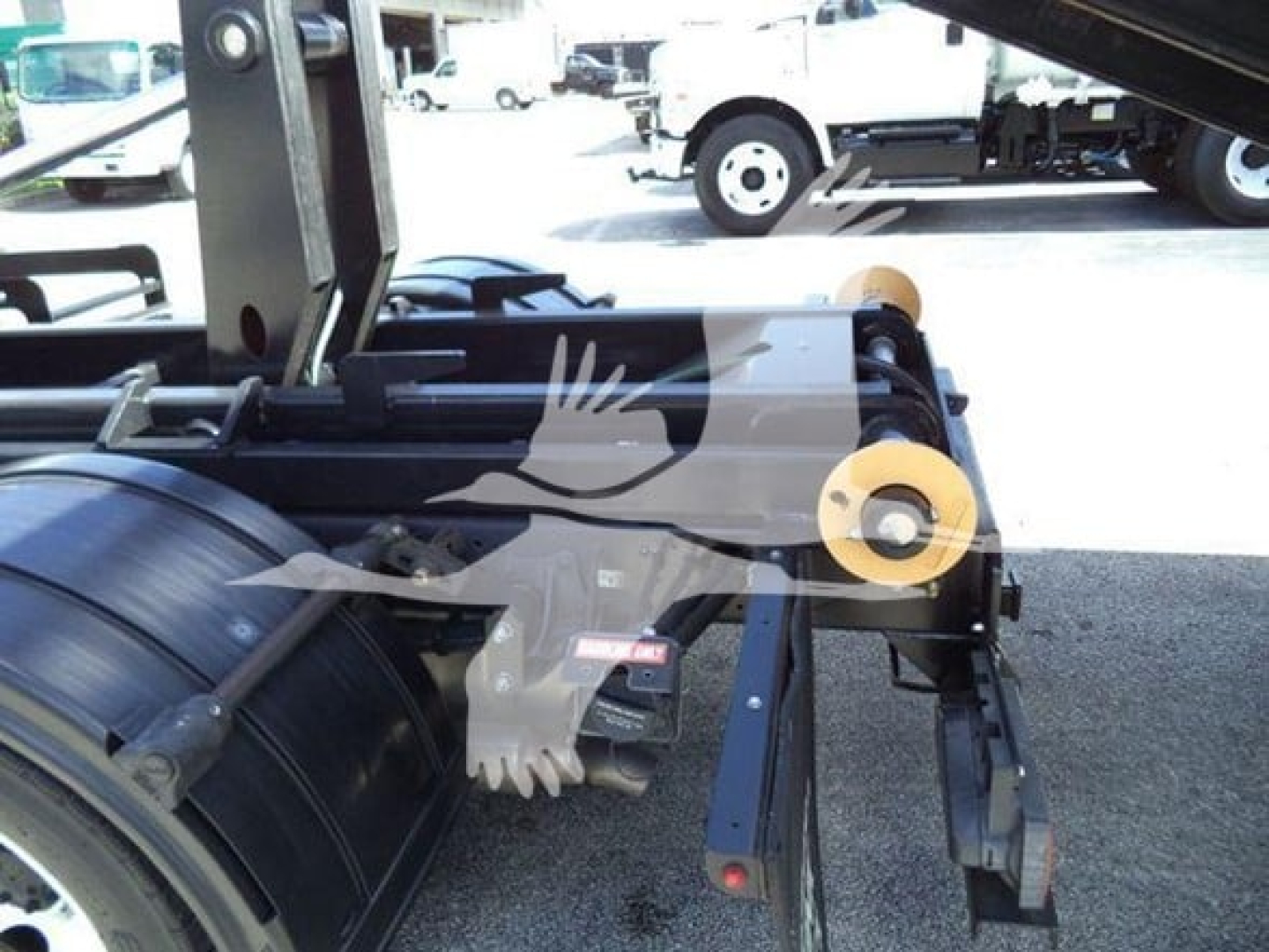 Isuzu NPR-HD truck area showing hooklift equipment with hydraulic cylinder, rollers, and yellow rollers on a black metal frame.
