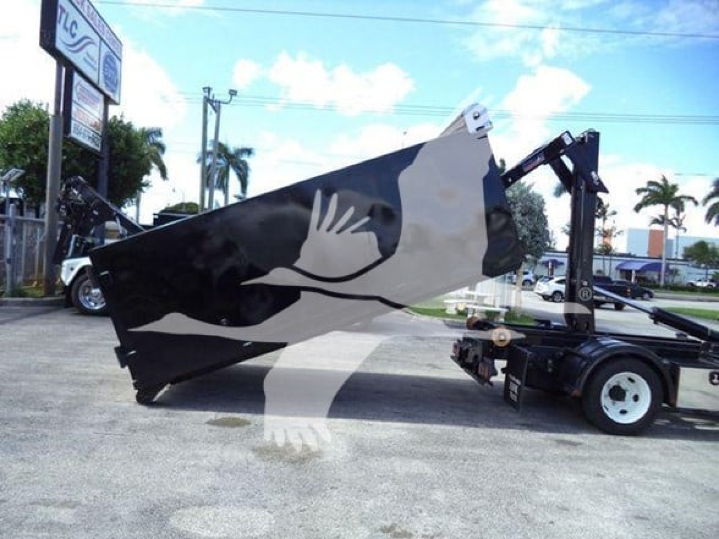 Isuzu NPR-HD truck with a hooklift system, black-and-white graphic on the side of the large cargo body, hydraulic arm and wheel setup visible.