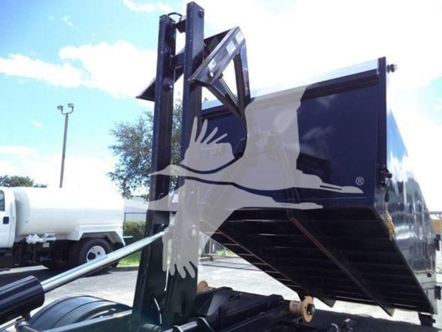 Isuzu NPR-HD truck with hooklift bed and hydraulic arm, side view showing cargo hopper and lifting mechanism.