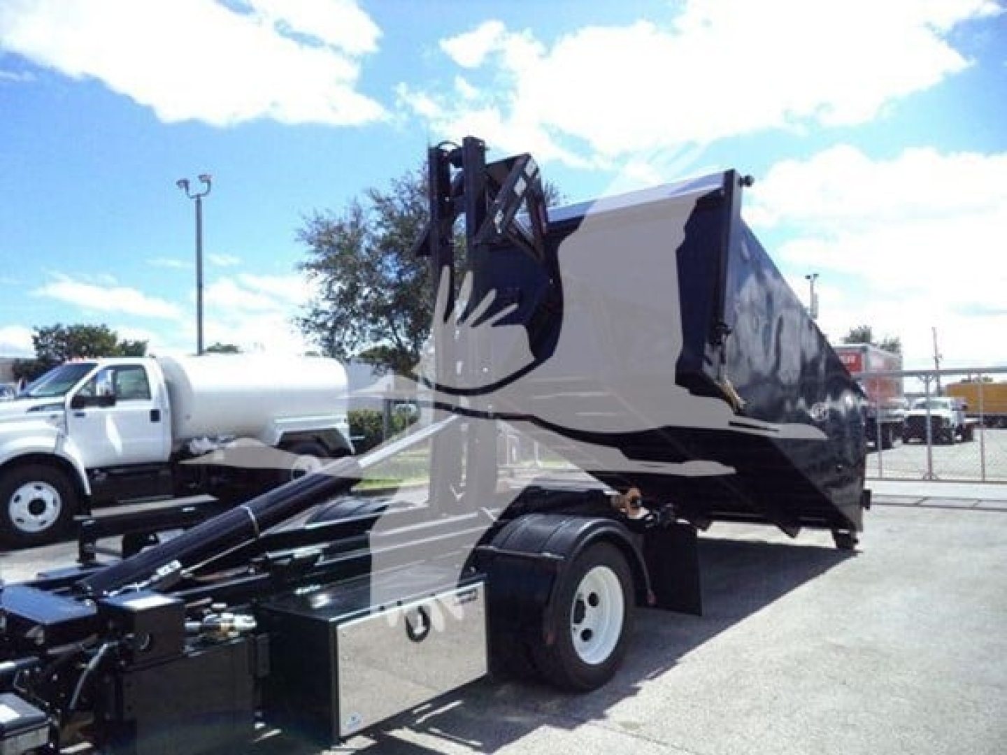 Isuzu NPR-HD truck with a black dump bed and hooklift attachment in a lot.