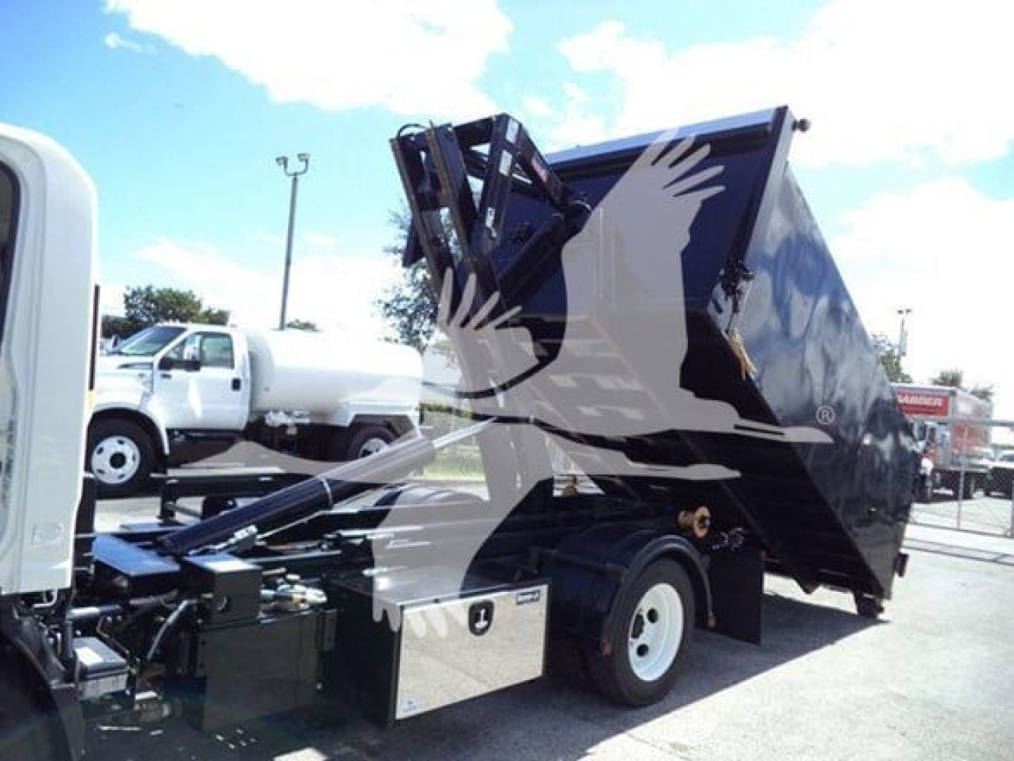 Isuzu NPR-HD truck with a raised hooklift bed in a side view showing a black dump body and chassis under bright sky.