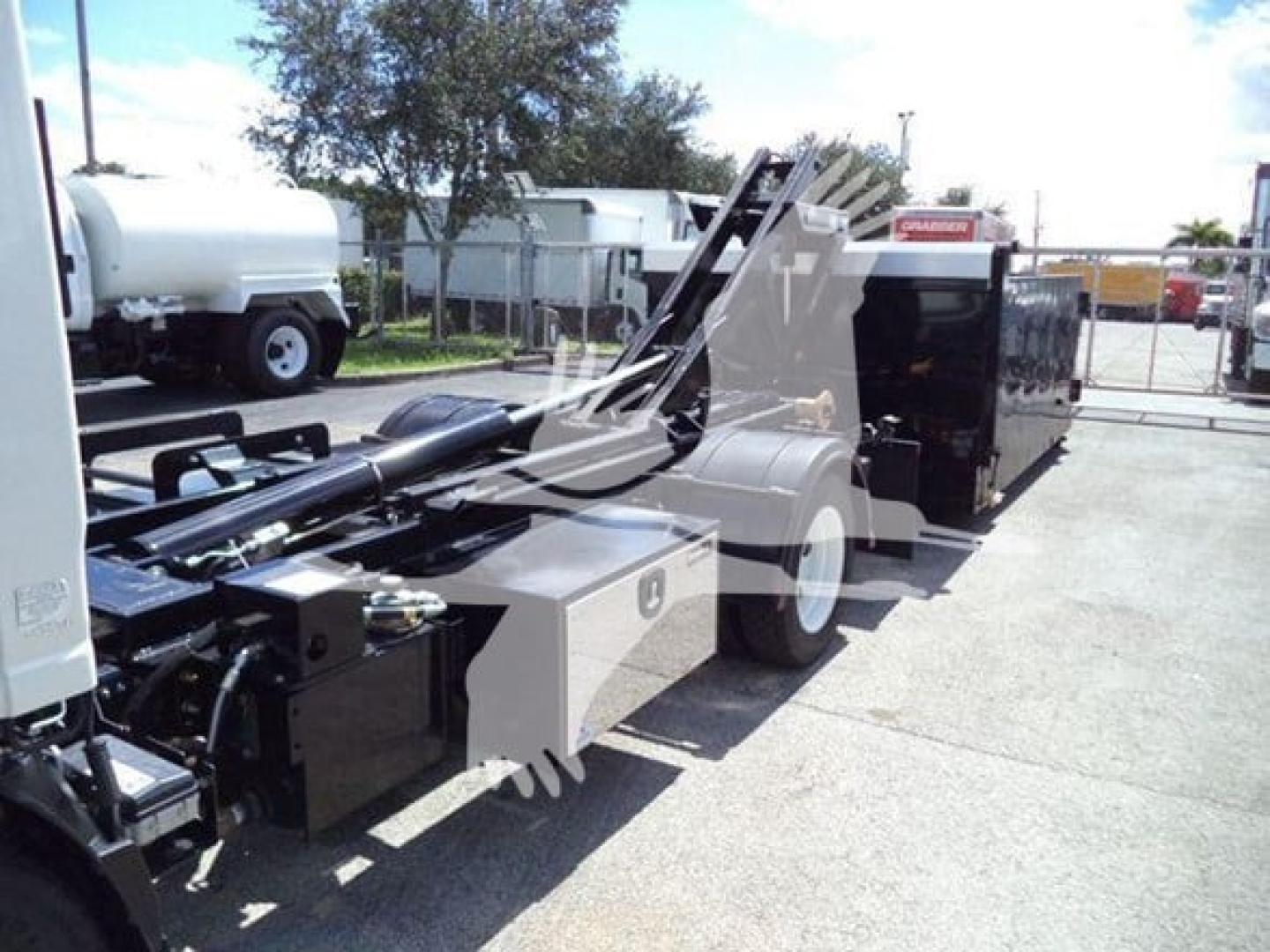Isuzu NPR HD hooklift truck chassis showing hydraulic arm and control unit, with fuel tank and framework visible.
