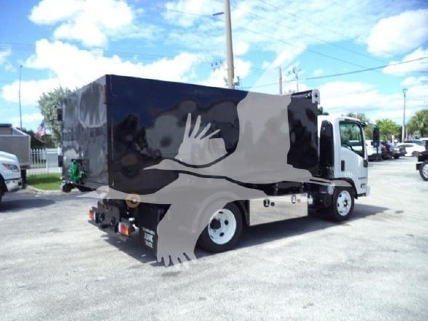Isuzu NPR-HD truck with a large black cargo box in the back, side view showing rear wheels and compact cab.