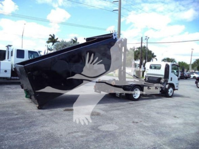 Isuzu NPR-HD truck with a large black hooklift bed, side view showing hoisted container and white cab, dealership lot in background.