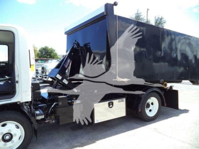 Isuzu NPR HD hooklift truck with a black dump body. Visible labels include no explicit text legibly, but the vehicle shows a white cab and black cargo area with hydraulic components near the chassis.