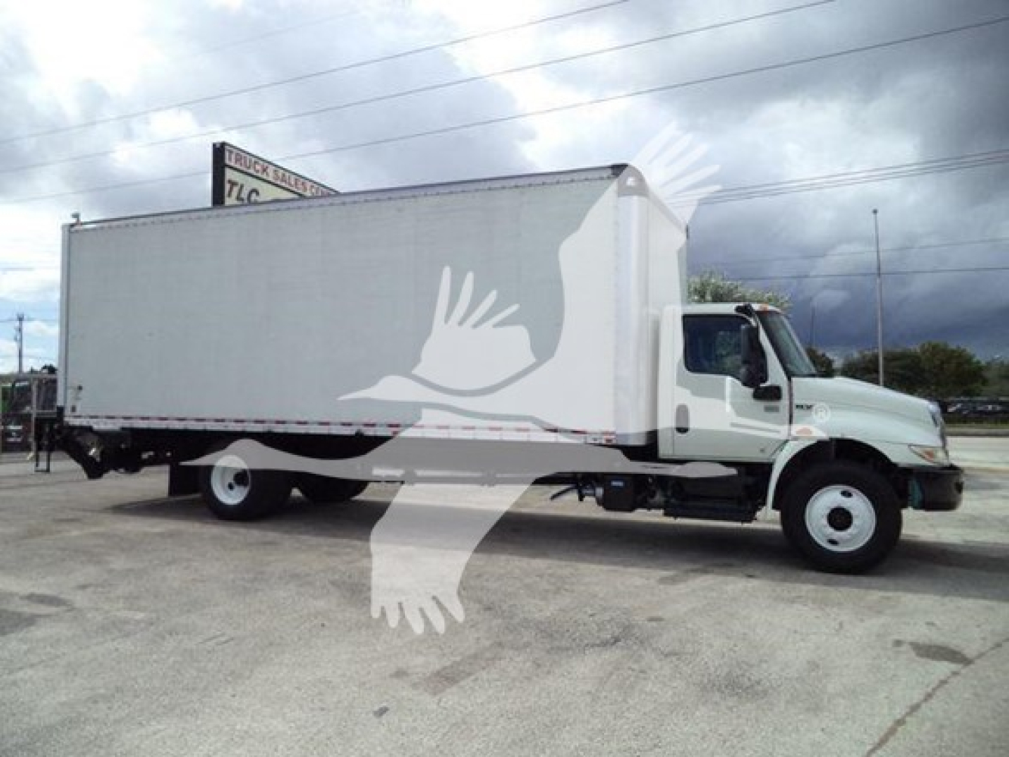 Box truck from a side angle showing a large cargo box on a sleeper cab Volvo? shell with plain white side, International MV model.