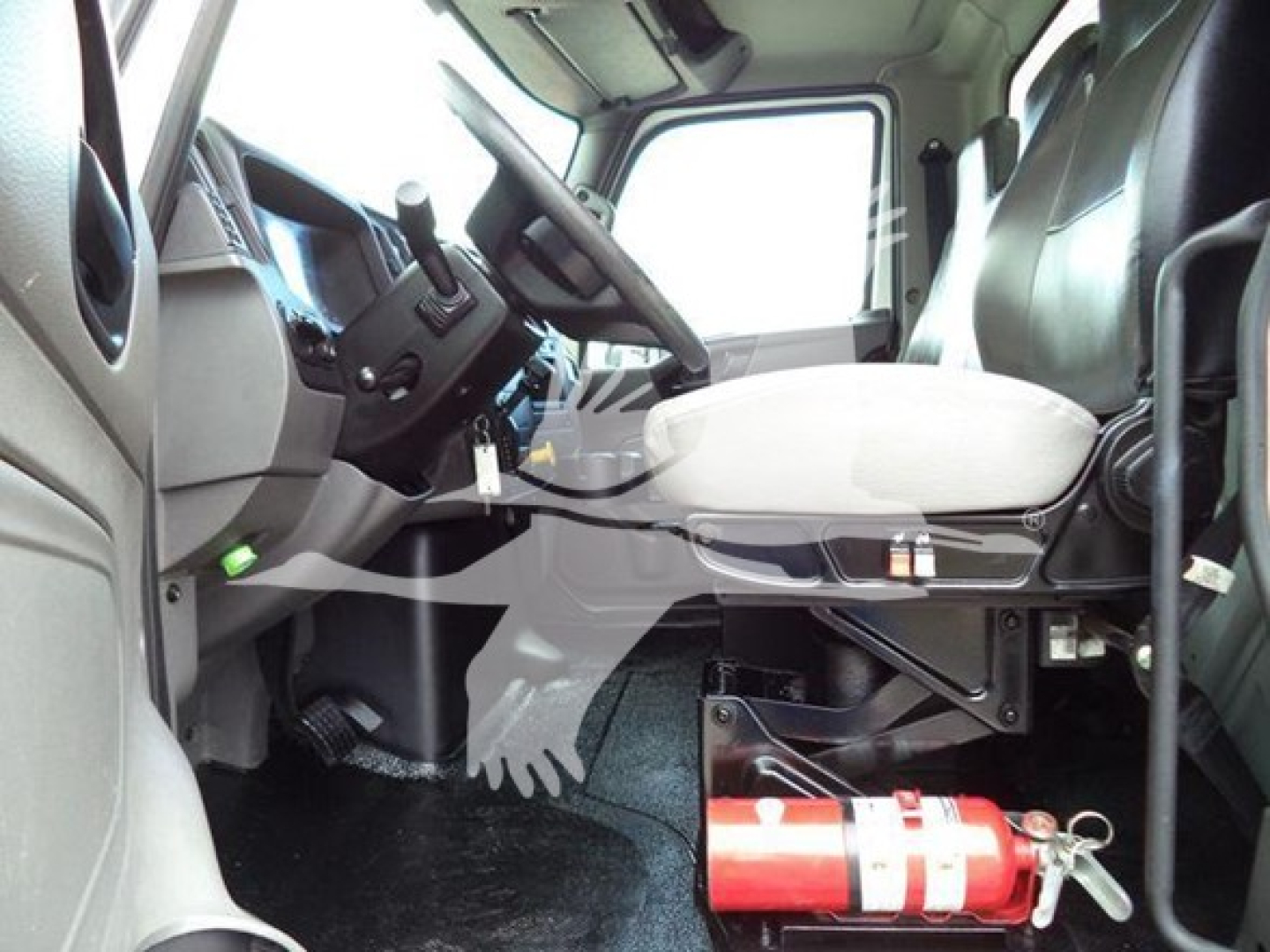 Interior cab of a used 2020 International MV truck showing driver's seat, steering column, dashboard, and a red fire extinguisher mounted under the seat.