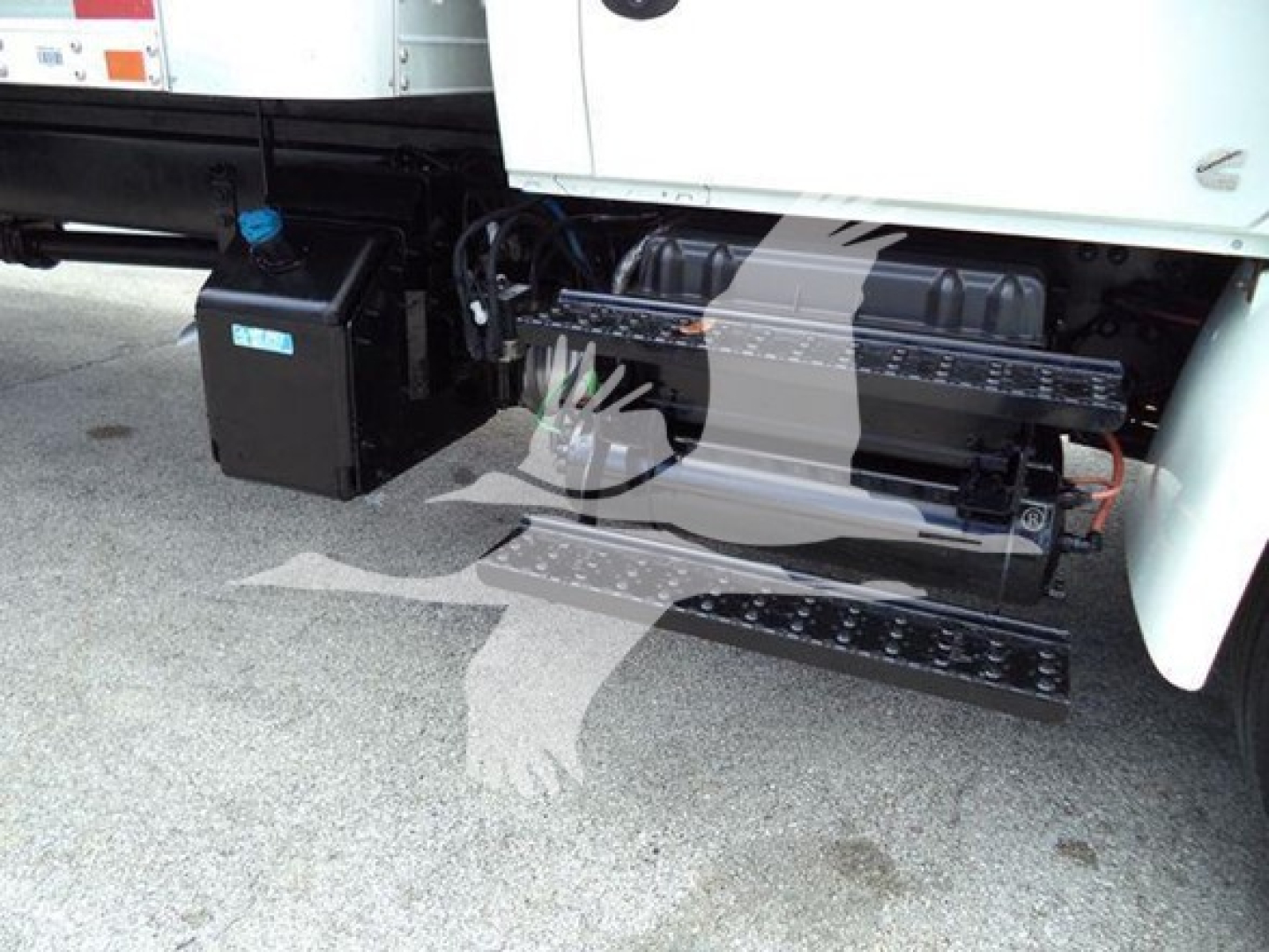 Truck side showing steps and fuel/electrical components under the cab with a black battery box and hydraulic lines.