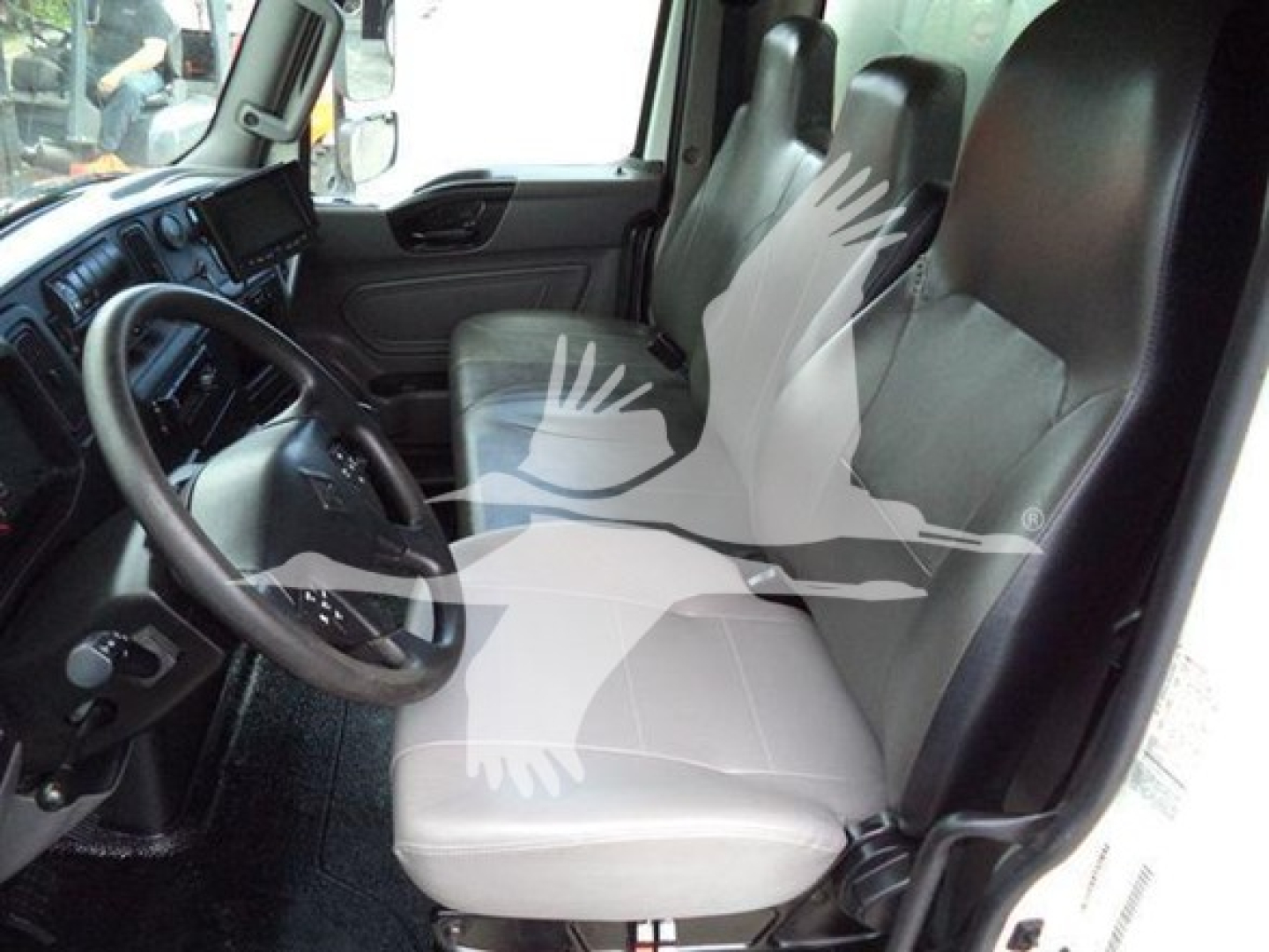 Interior cab view of a 2020 International MV truck showing front driver seat, steering wheel, dashboard, and passenger seat with light gray upholstery.