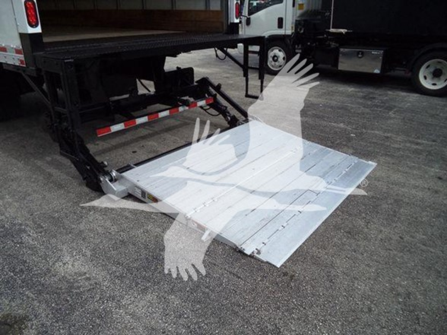 Platform/ramps of a truck with a metal lift gate deployed from the back of a flatbed unit. Mounted metal plate with ribbed surface and hydraulic lift mechanism visible.