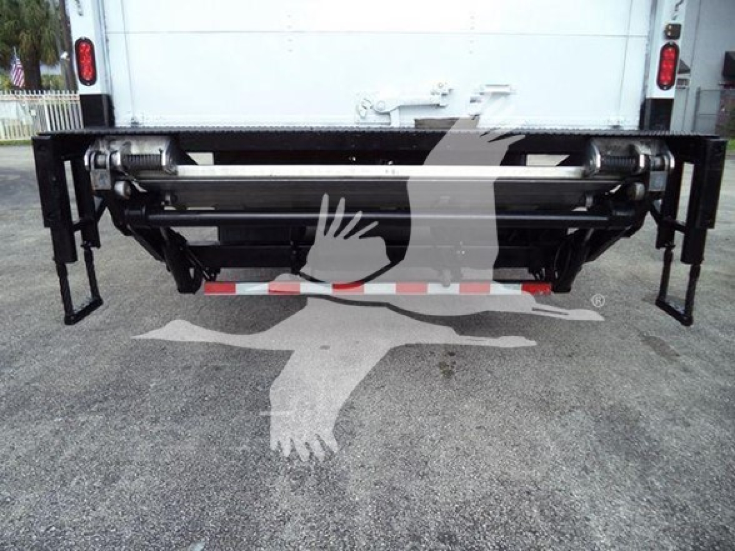 Back end of a box truck with a large rear bumper and a heavy-duty under-vehicle lift/roller assembly visible.