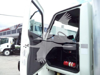 Truck cab interior showing open door with dashboard and a red fire extinguisher in the footwell. Exterior shows another truck in background.