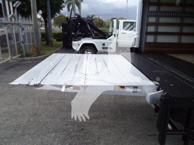 Flatbed truck bed with white metal platform extending from a tow truck in a yard.