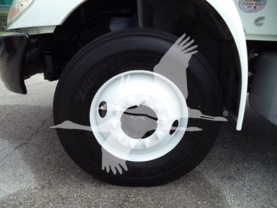 Truck front wheel and fender showing wheel, tire, and white rim with partial side of cab and sticker in background.
