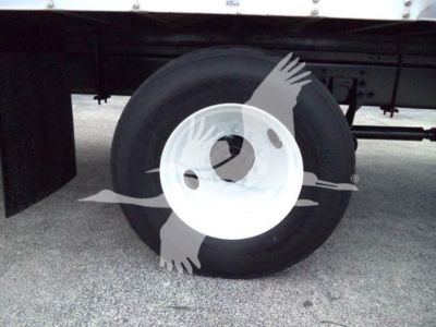 Truck wheel with white rim and black tire under a box truck; faint watermark overlays the image.