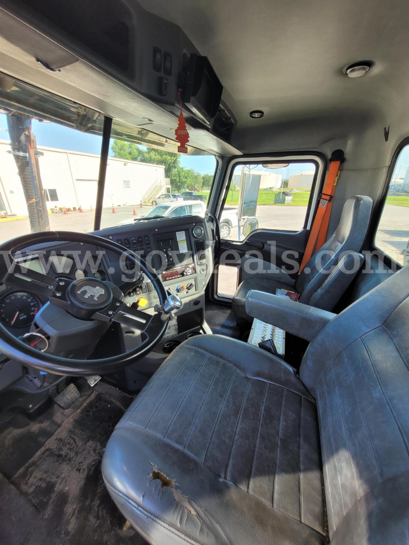 Cab interior of a 2017 Mack GU713 truck showing steering wheel, dashboard, driver seat with wear, and gray fabric seats.