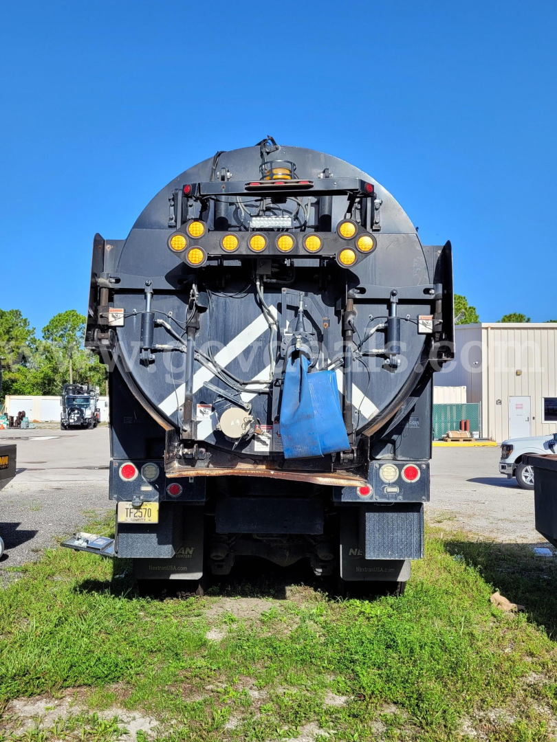 Rear view of a Mack GU713 vacuum truck showing circular rear body, multiple yellow lights, hoses, and access panels.