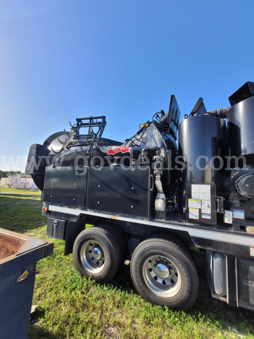 Mack GU713 vacuum truck side view showing equipment and hydraulic components with wheel set and black body