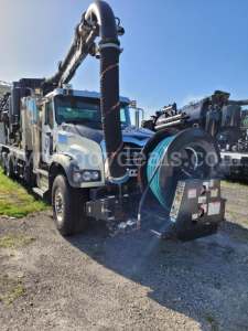 Mack GU713 vacuum truck with large cylindrical vacuum hose and booster unit mounted on chassis; VIN plate and stock number not visible.