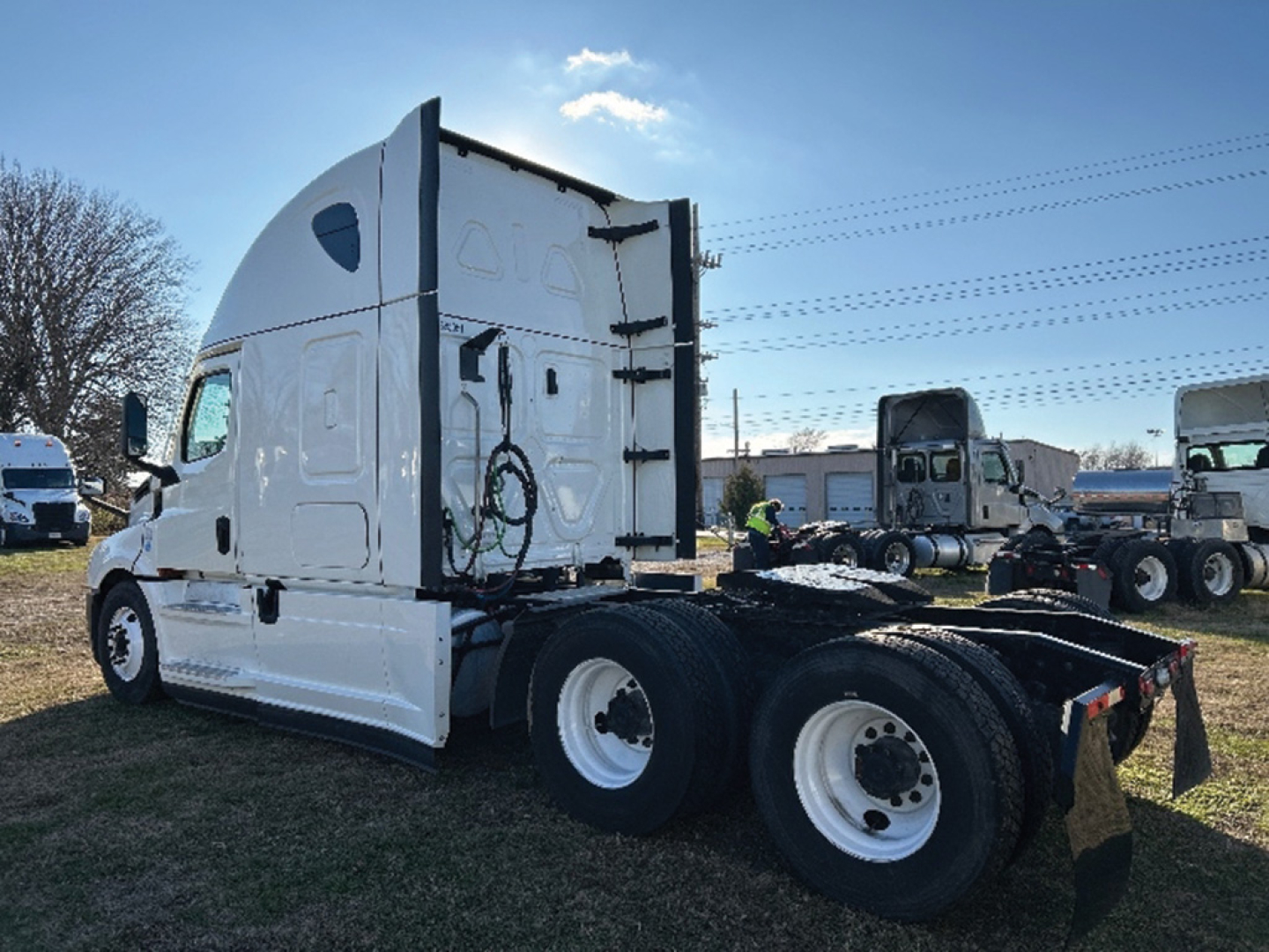 Freightliner Cascadia126 truck cab and chassis from rear-left side showing sleeper cab, tandem axle rear with white wheels, fifth wheel area, and surrounding equipment.