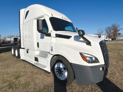 Freightliner Cascadia126 truck in a lot viewed from the front-left, white cab with grey front bumper, sleeper cab silhouette, dual rear wheels visible.