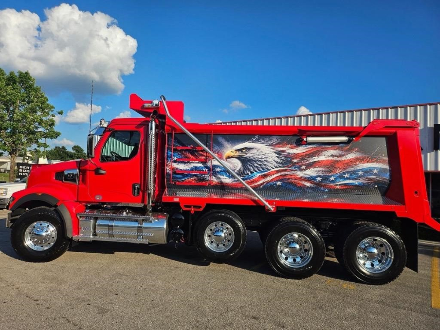 Dump truck side view showing red 2026 Western Star 49X with patriotic eagle mural on the dump body.