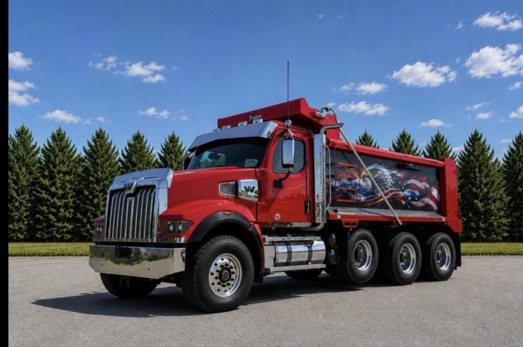 Dump truck showing Western Star 49X with red chassis and graphic dump bed in an open lot.