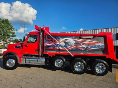 Dump truck side view showing red 2026 Western Star 49X with patriotic eagle mural on the dump body.