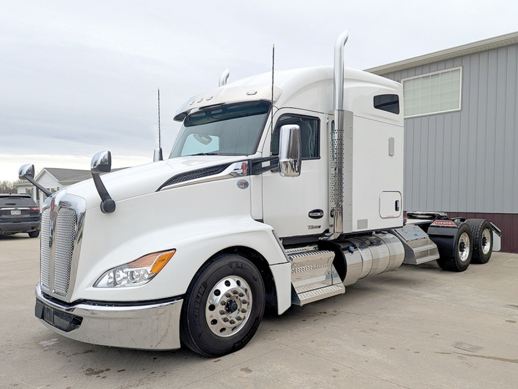 Kenworth T680 Next Gen sleeper tractor in white with side exhausts, showing chrome fuel tanks and dual rear axles.