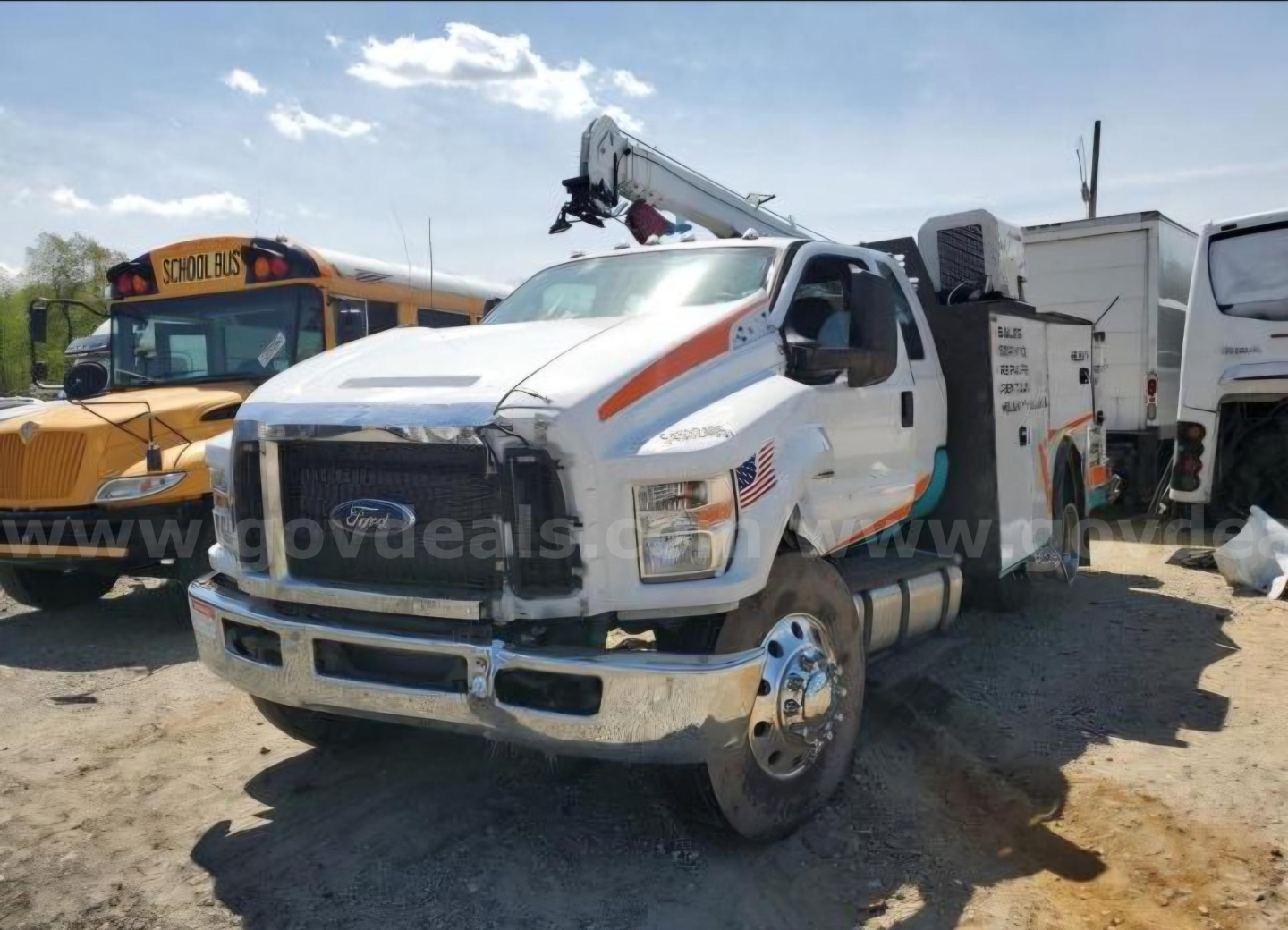 Ford F-750 utility/service truck with crane mounted in bed, side view showing front grille and wheel; American flag decal on door; other service trucks in background.