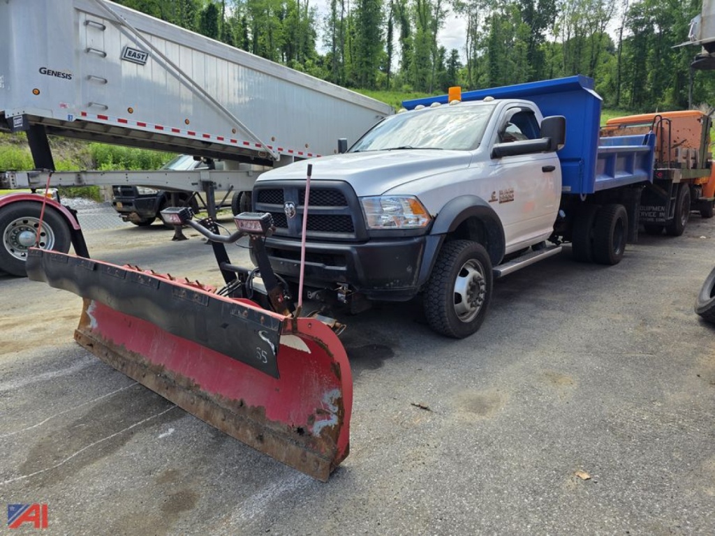 Ram 5500 dump truck with plow attachment in a yard; snow plow at front, dump bed in blue, multiple trailers in background.