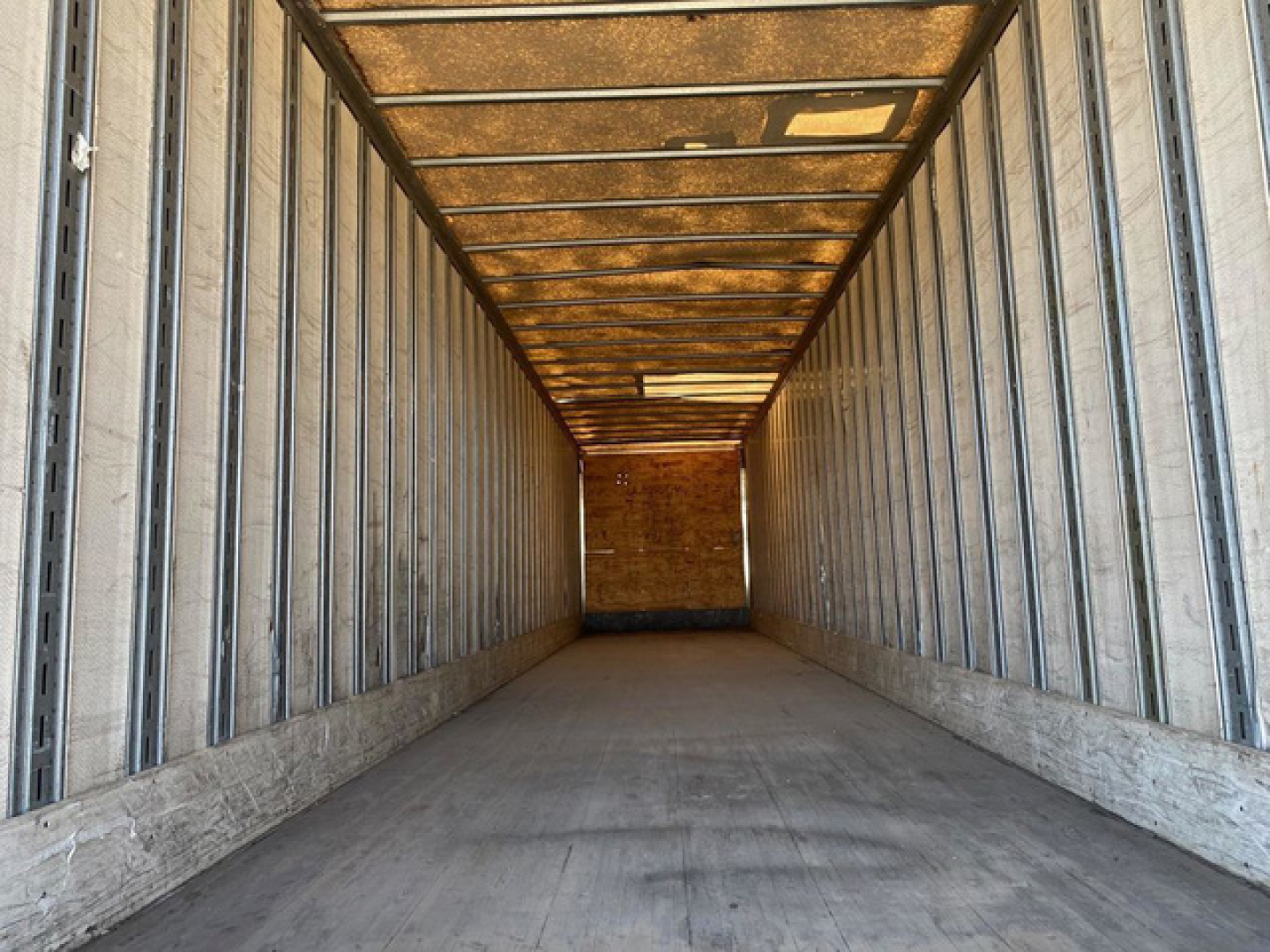 Van trailer interior showing empty cargo area with metal wall studs and overhead roof beams.