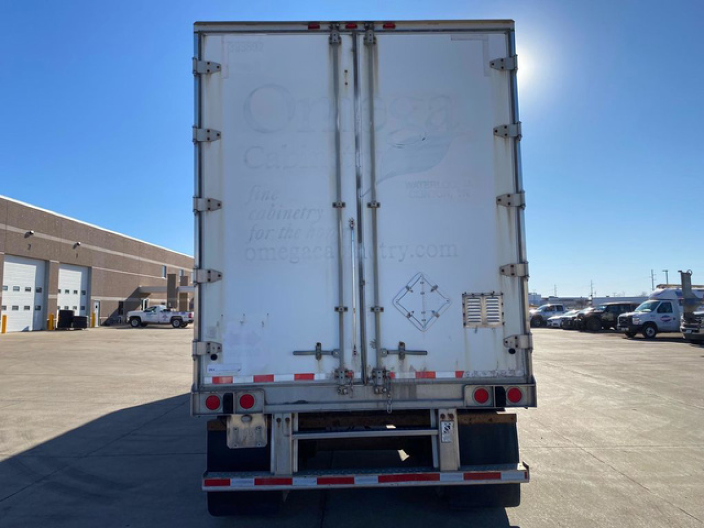 Rear view of a white Great Dane van trailer with two rear doors, taillights, and a metal bumper. Faint text on doors, reflective stripes along bottom, forklift-holding area.