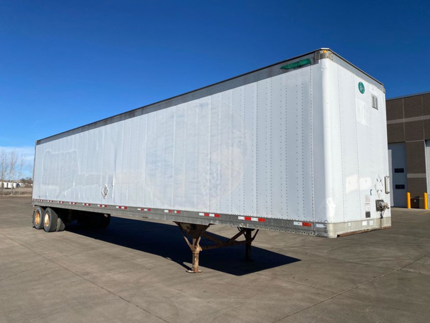 Trailer body showing a long silver Great Dane van trailer with support legs and dual rear doors in an outdoor lot.