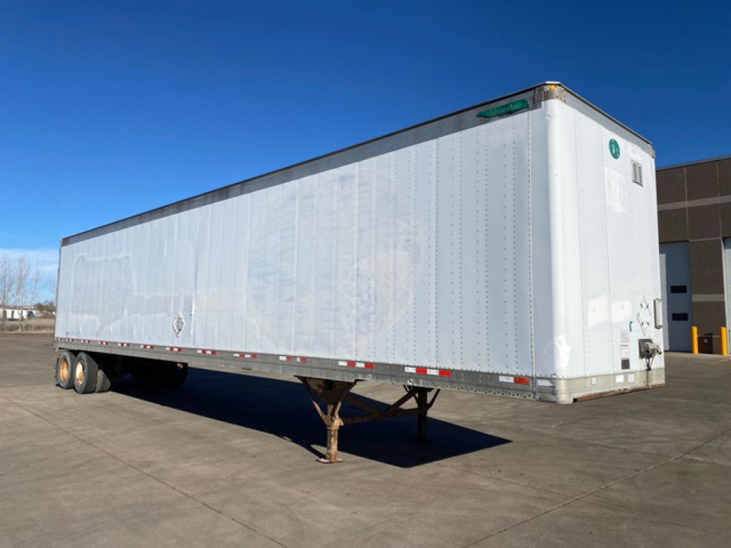 Trailer body showing a long silver Great Dane van trailer with support legs and dual rear doors in an outdoor lot.