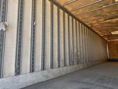 Rear interior of a Great Dane trailer with corrugated metal side walls and wood roof, empty cargo area, concrete floor, and daylight at the far end.