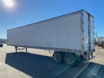 Great Dane trailer with a long rectangular cargo area, rear doors, dual rear axles, parked on a lot. No visible text readable on the side, some light reflections.