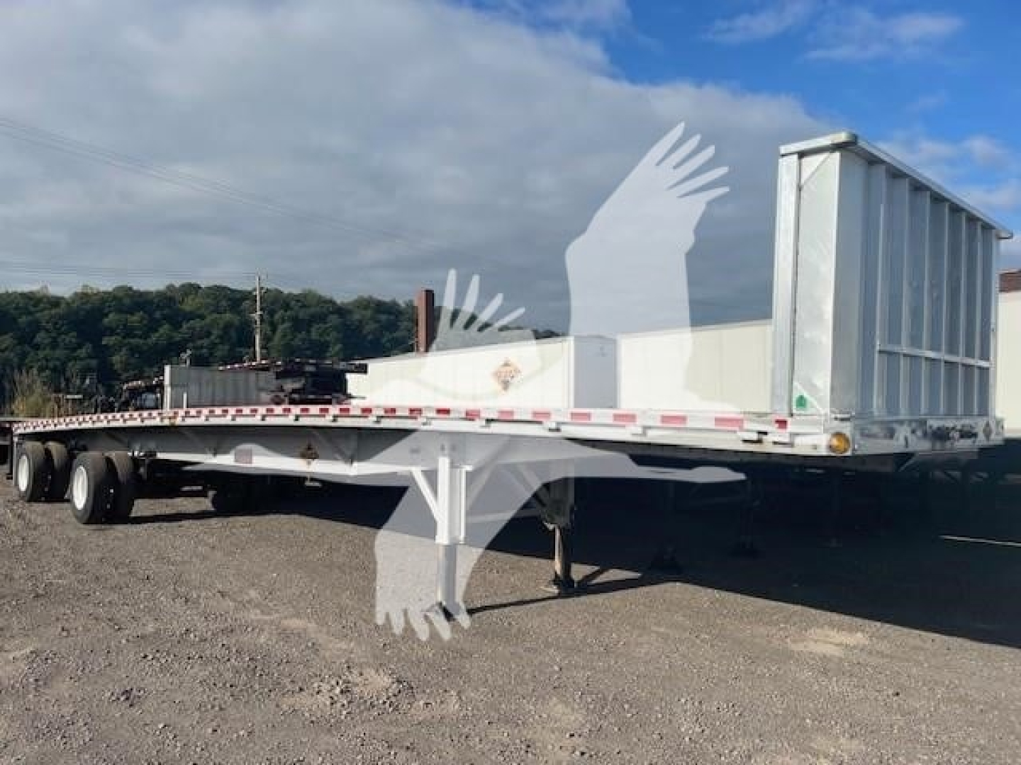 Flatbed trailer showing rear and side view with a raised gooseneck, aluminum flatbed, white reflective tape, and multiple axles; 2020 Reitnouer Big Bubba trailer.