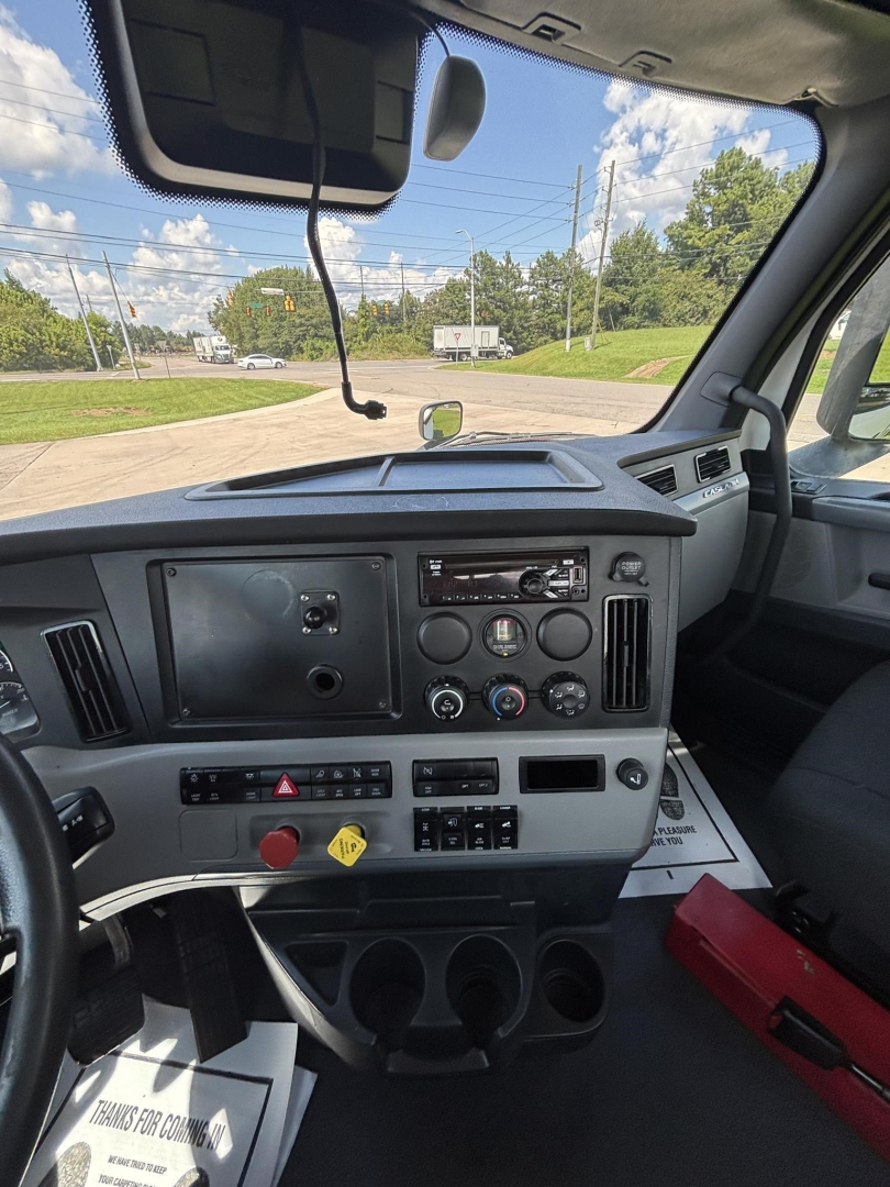Dashboard of a Freightliner Cascadia 126 cab showing instrument panel, steering column, center console, and windshield with road outside.