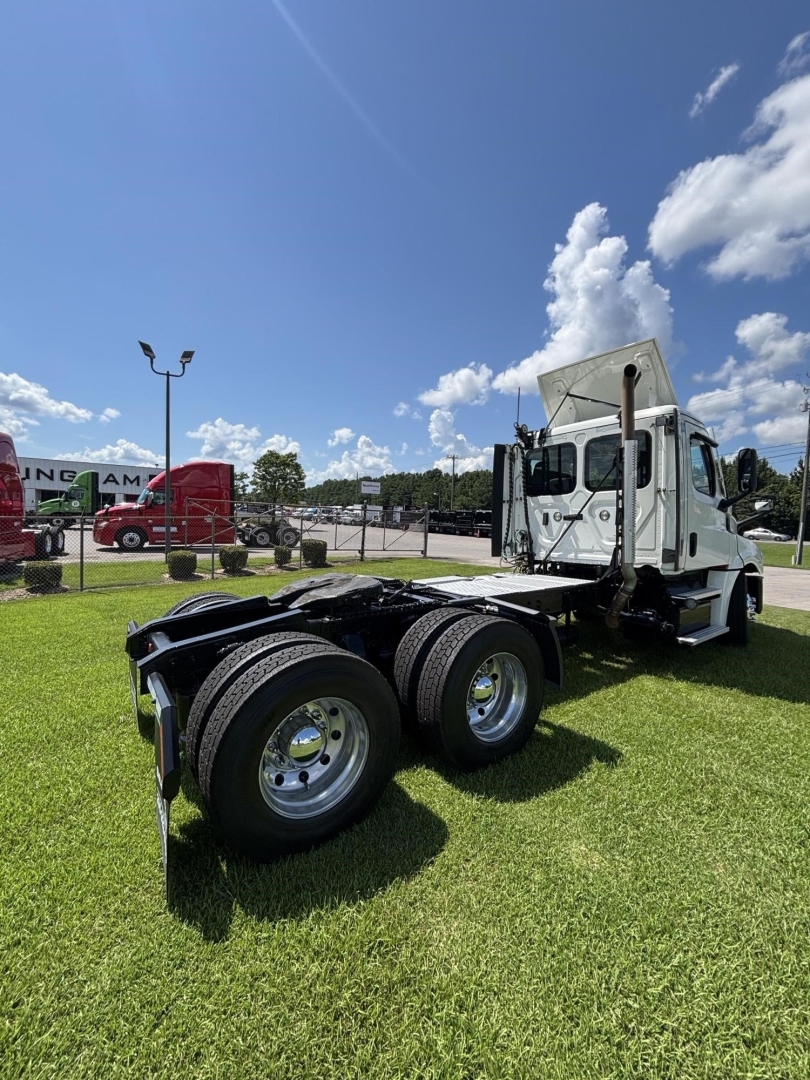 Freightliner Cascadia 126 day cab tractor chassis with dual rear axles and white cab, clear sky, grassy lot.