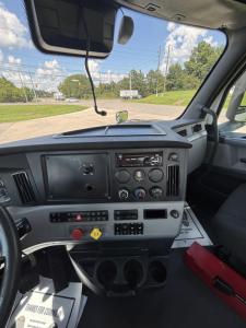 Dashboard of a Freightliner Cascadia 126 cab showing instrument panel, steering column, center console, and windshield with road outside.