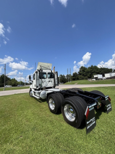 Truck at an outdoor lot showing a Freightliner Cascadia 126 tractor from rear three-quarter view; dual rear axles, fifth wheel, mud flaps, and white cab with large mirrors.