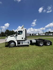 Truck chassis with cab of a 2021 Freightliner Cascadia 126 tractor, side view showing dual rear axles, chrome fuel tanks, and side steps.