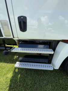 Truck side view showing metal retractable steps under door of a Freightliner Cascadia day cab.